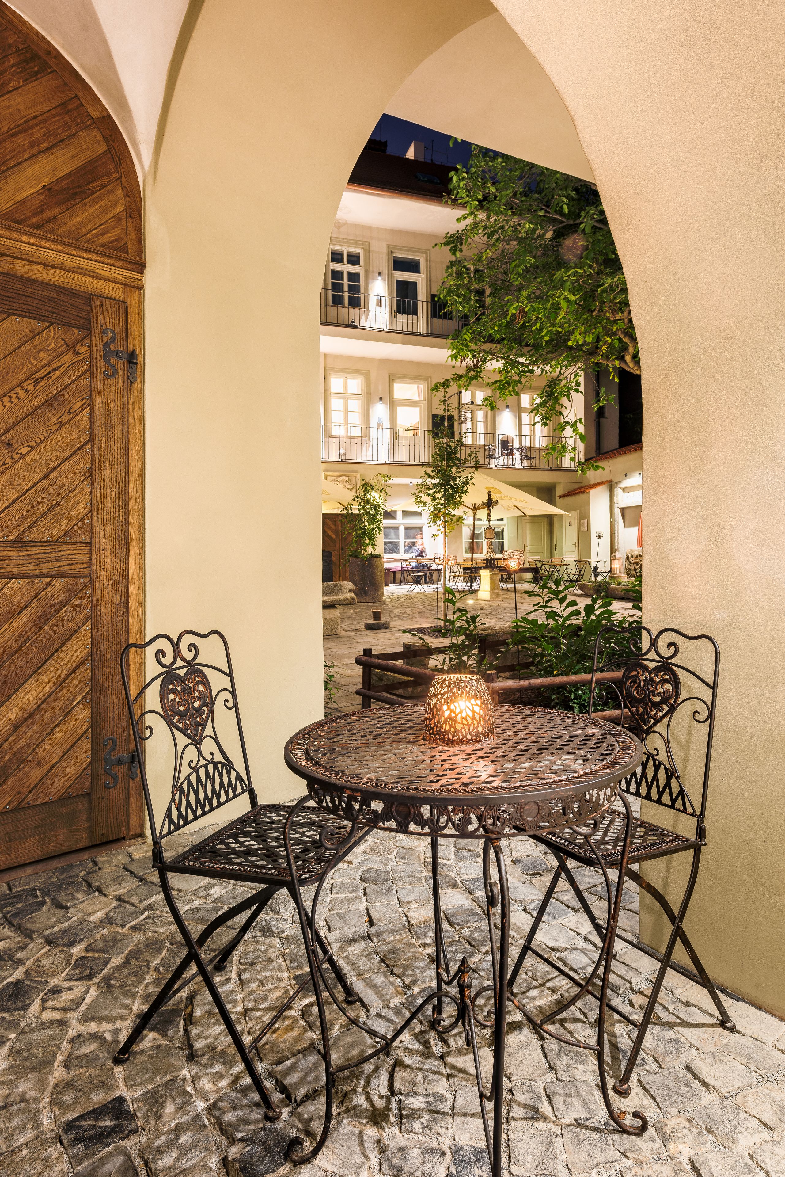 Un cortile con un tavolo e sedie in metallo rotondo, una porta in legno e vista sull'interno dell'edificio.