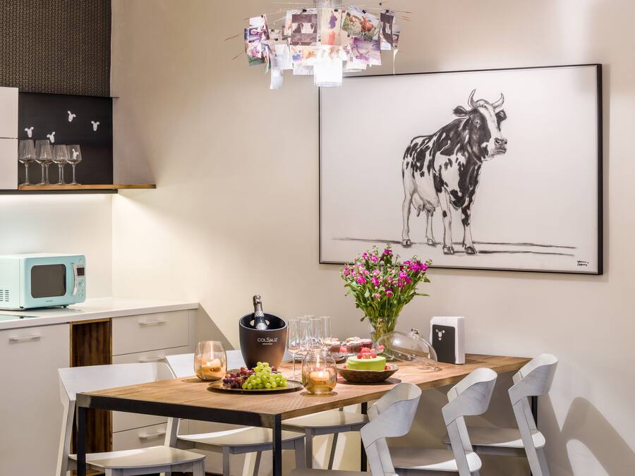 Un comedor con una mesa de madera, sillas blancas, un microondas azul y una obra de arte enmarcada de una vaca.