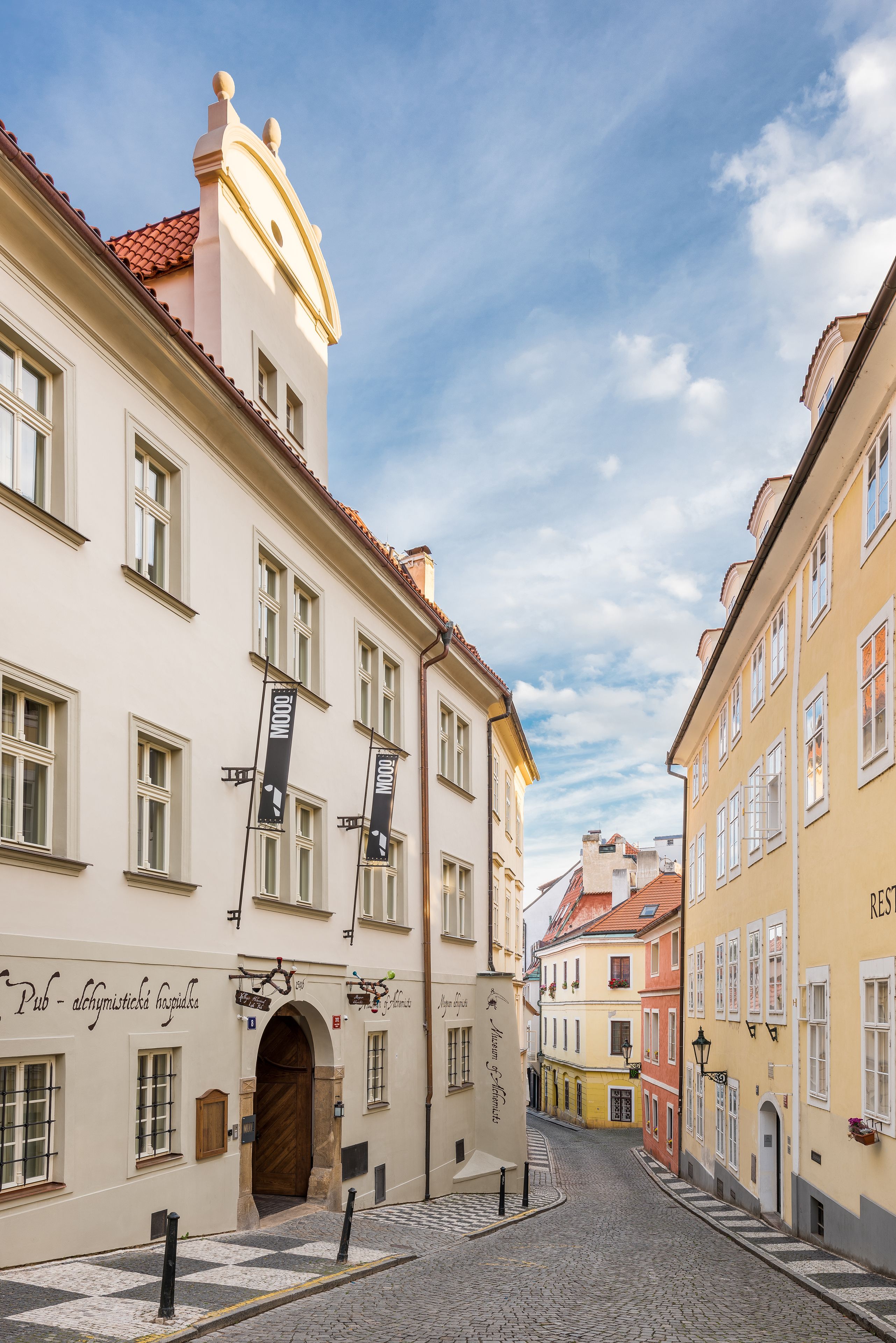 A cobblestone street with historic buildings, a pub sign, and a clear sky.