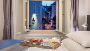 A bedroom with a view of a street at dusk, a tray with breakfast items, and a lit candle on the bed. - MOOo by the Castle (Prague)