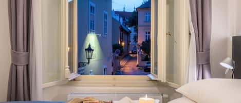 A bedroom with a view of a street at dusk, a tray with breakfast items, and a lit candle on the bed.