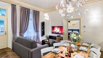 A modern living room with a sofa, dining table set for six, and a TV in the background.