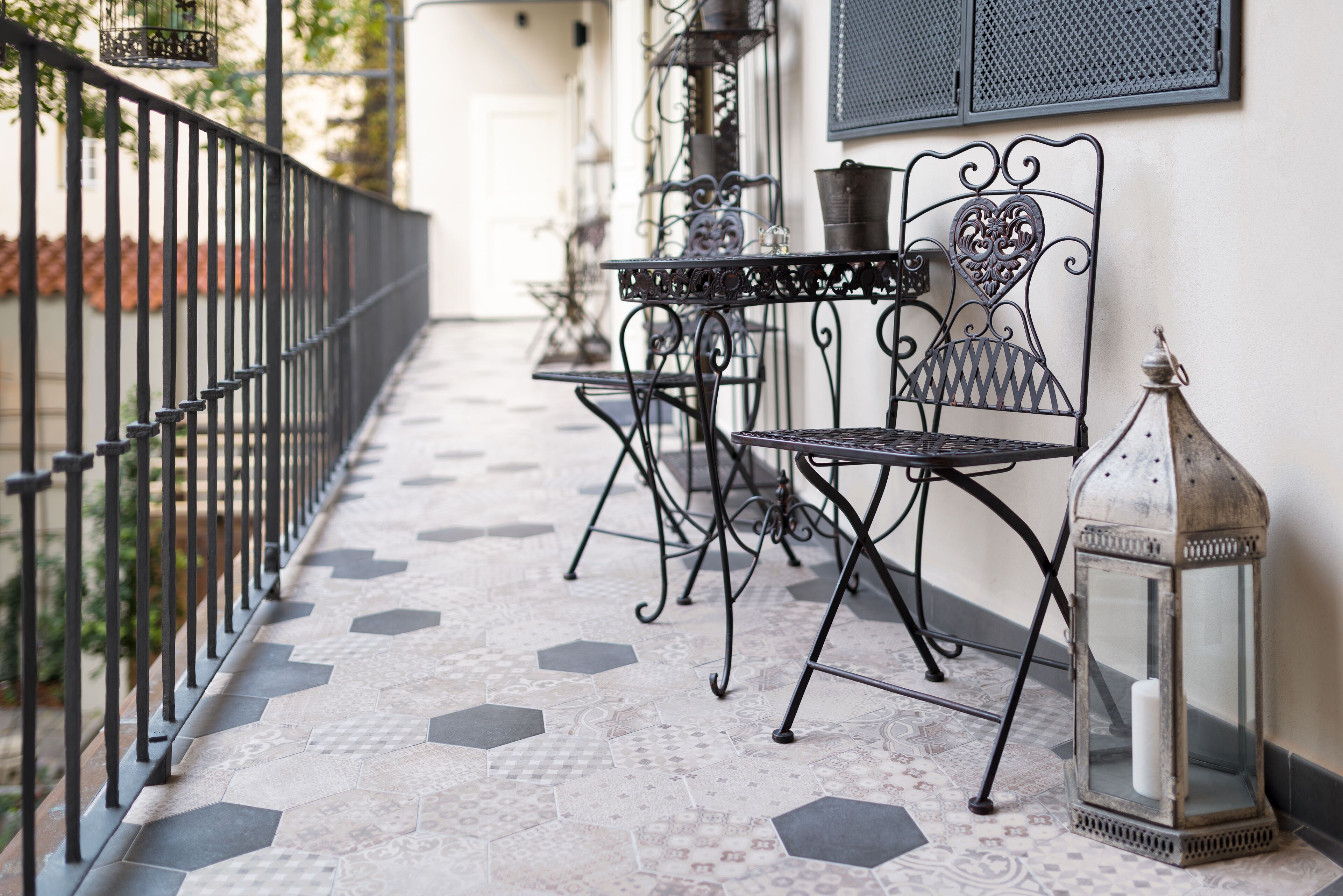Un balcon avec une table et des chaises en métal, une lanterne et un sol à motifs.