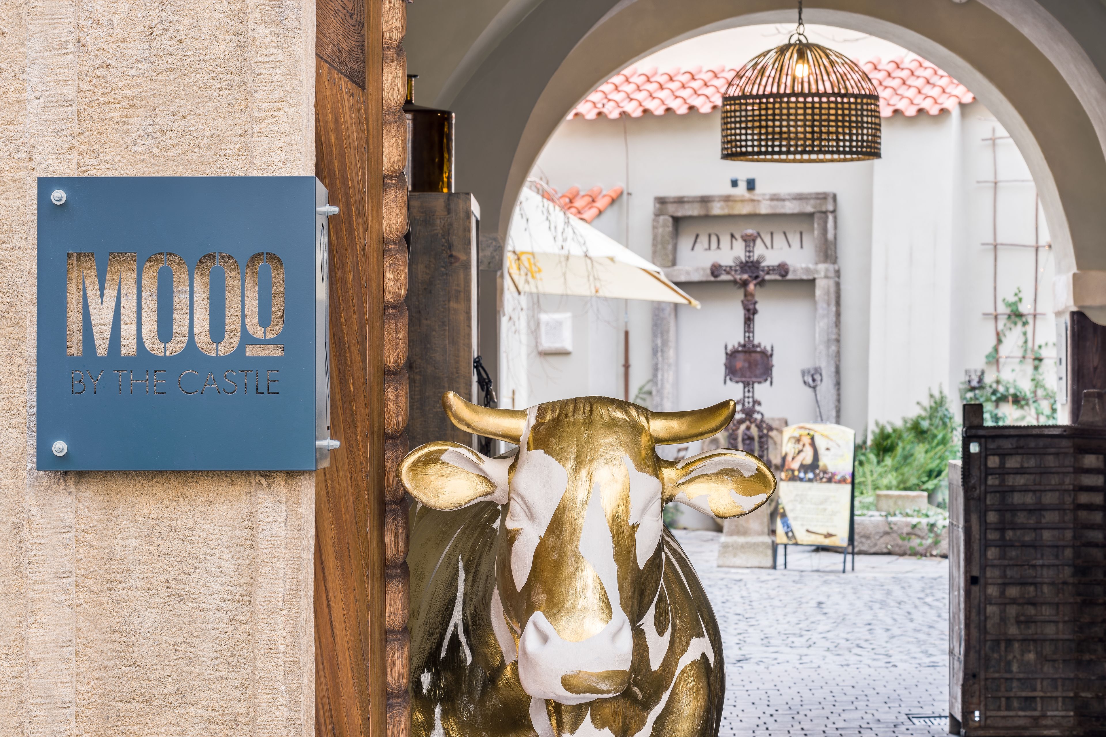 Un senyal amb la inscripció 'MOOO BY THE CASTLE' i una estàtua daurada de vaca a l'entrada.