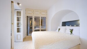 A bedroom with a large bed, a wardrobe, and an arched doorway. - Hyperion Oia Suites (Santorini)