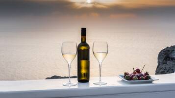 Una botella de vino y dos copas sobre una mesa con un plato de uvas, con vistas a un cuerpo de agua al atardecer.
