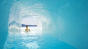 A person in a clear, blue, tunnel-like structure with a view of the sky and distant landscape. - Hyperion Oia Suites (Santorini)