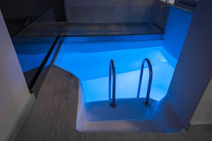 Un baño pequeño y moderno con bañera de hidromasaje con mampara de vidrio y suelo de madera.