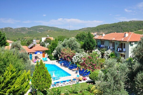 A pool area with lounge chairs and a building with a red-tiled roof. - Gorkem Hotel & Apartments (Fethiye)
