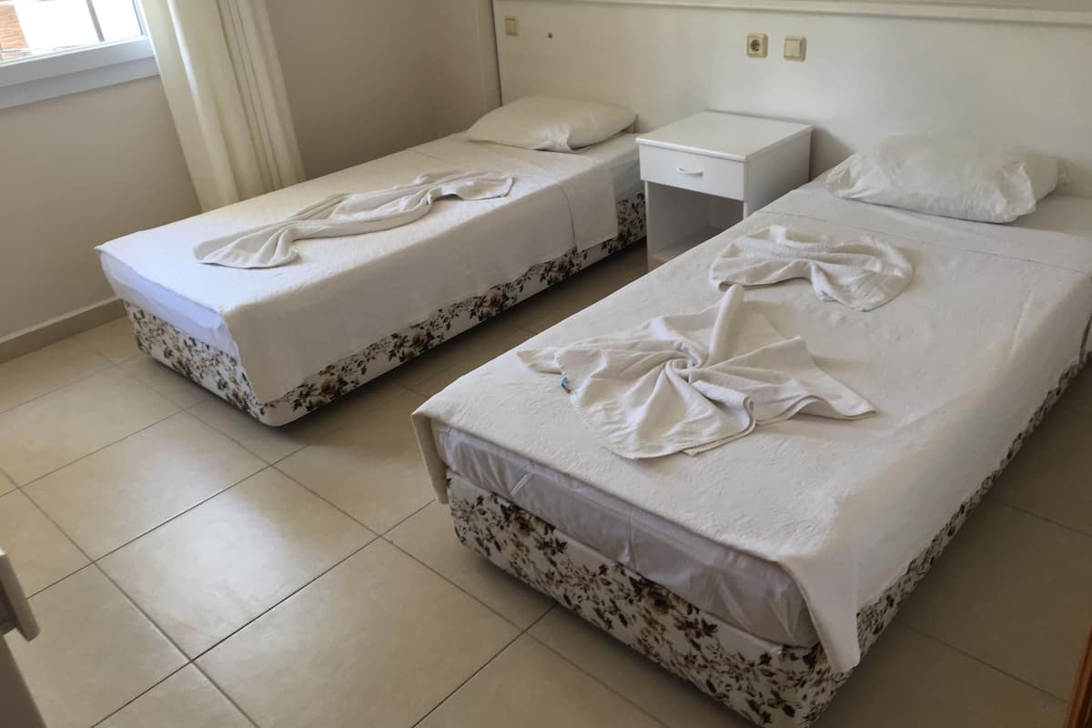 A hotel room with two single beds, a small bedside table, and a window with curtains.