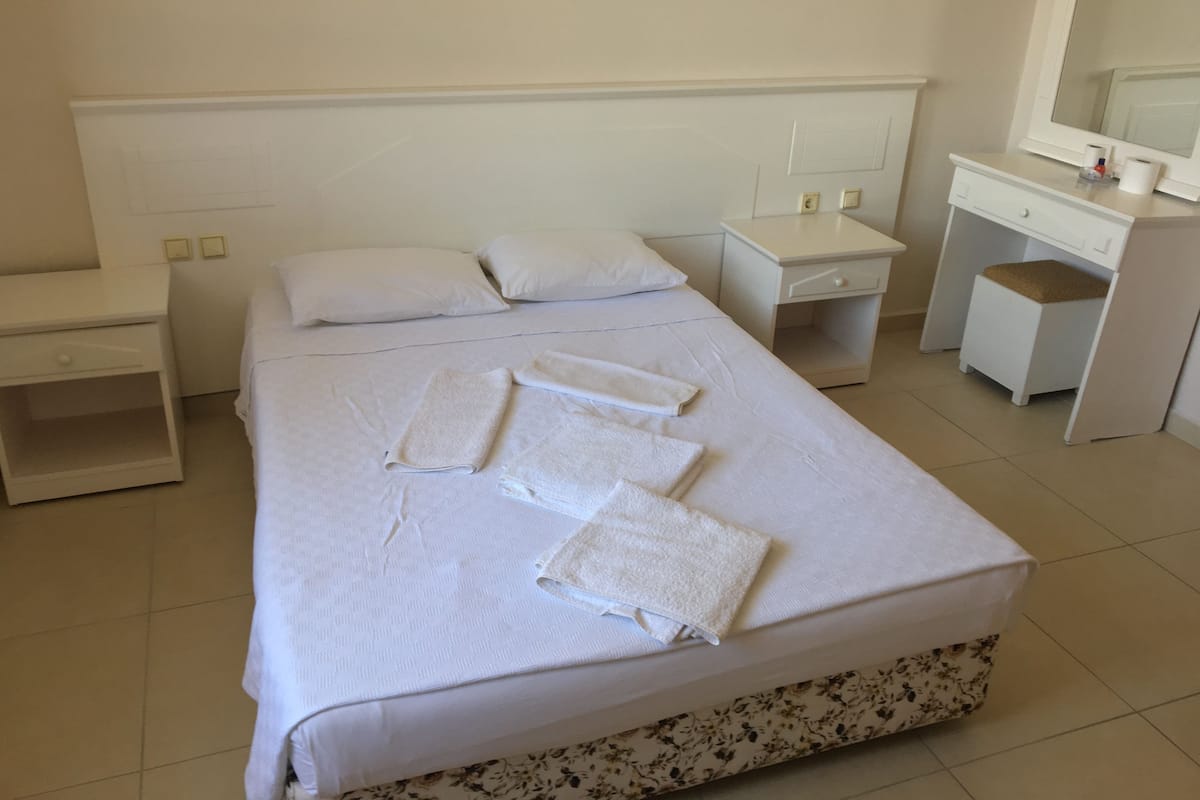 A neatly made bed with towels, a bedside table, a dresser, and a mirror.