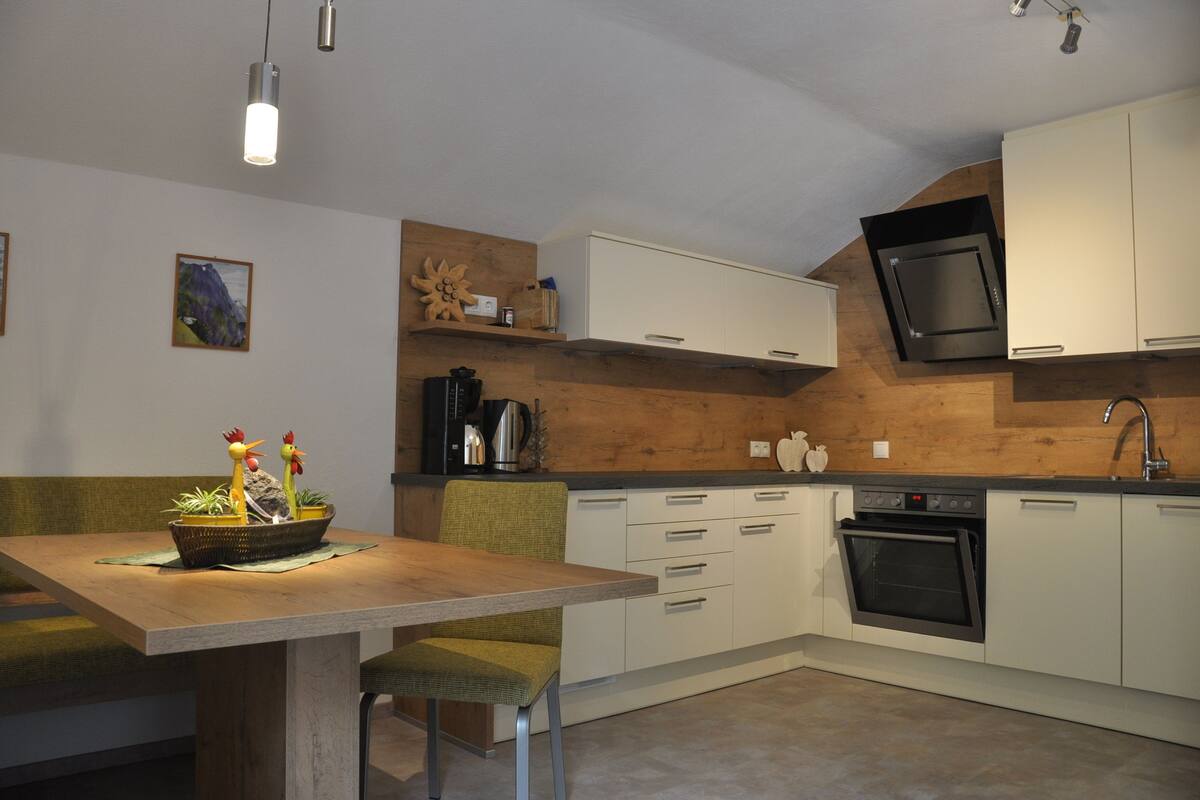 Een moderne keuken met witte kasten, een inbouwoven en een wand bekleed met hout.