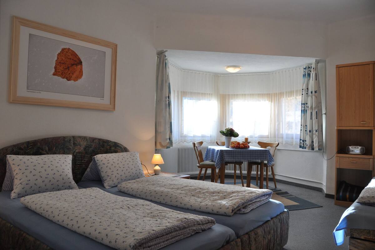 Een slaapkamer met twee bedden, een eettafel en een raam met gordijnen.