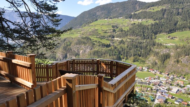A wooden deck overlooking a village with houses and mountains in the background.