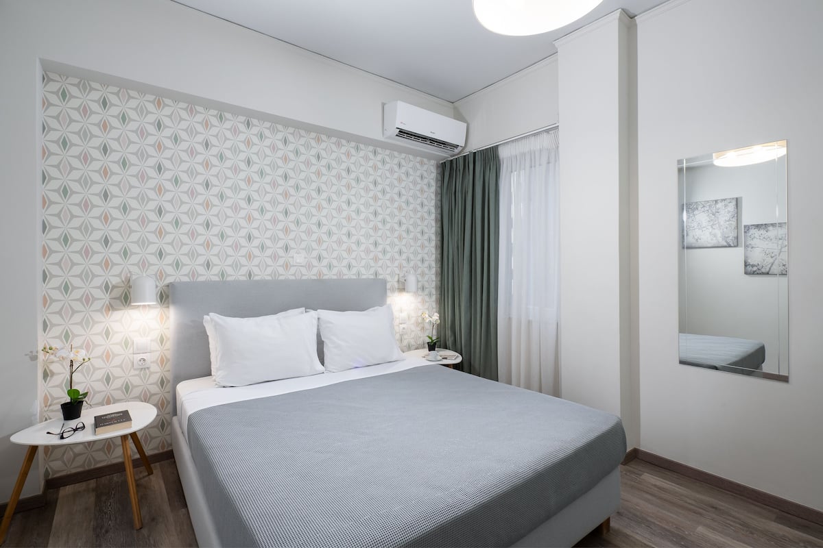 A neatly arranged hotel room with a bed, bedside tables, a small plant, and a wall-mounted air conditioner.