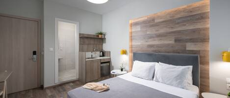 A modern hotel room with a bed, bedside table, and a small kitchenette.