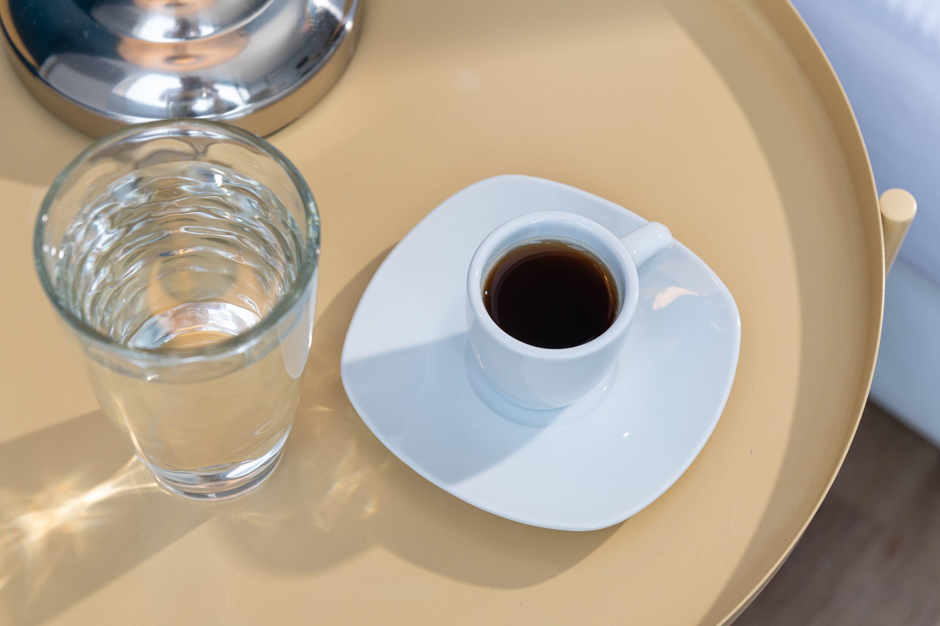 A tray with a glass of water and a cup of coffee on a beige table.