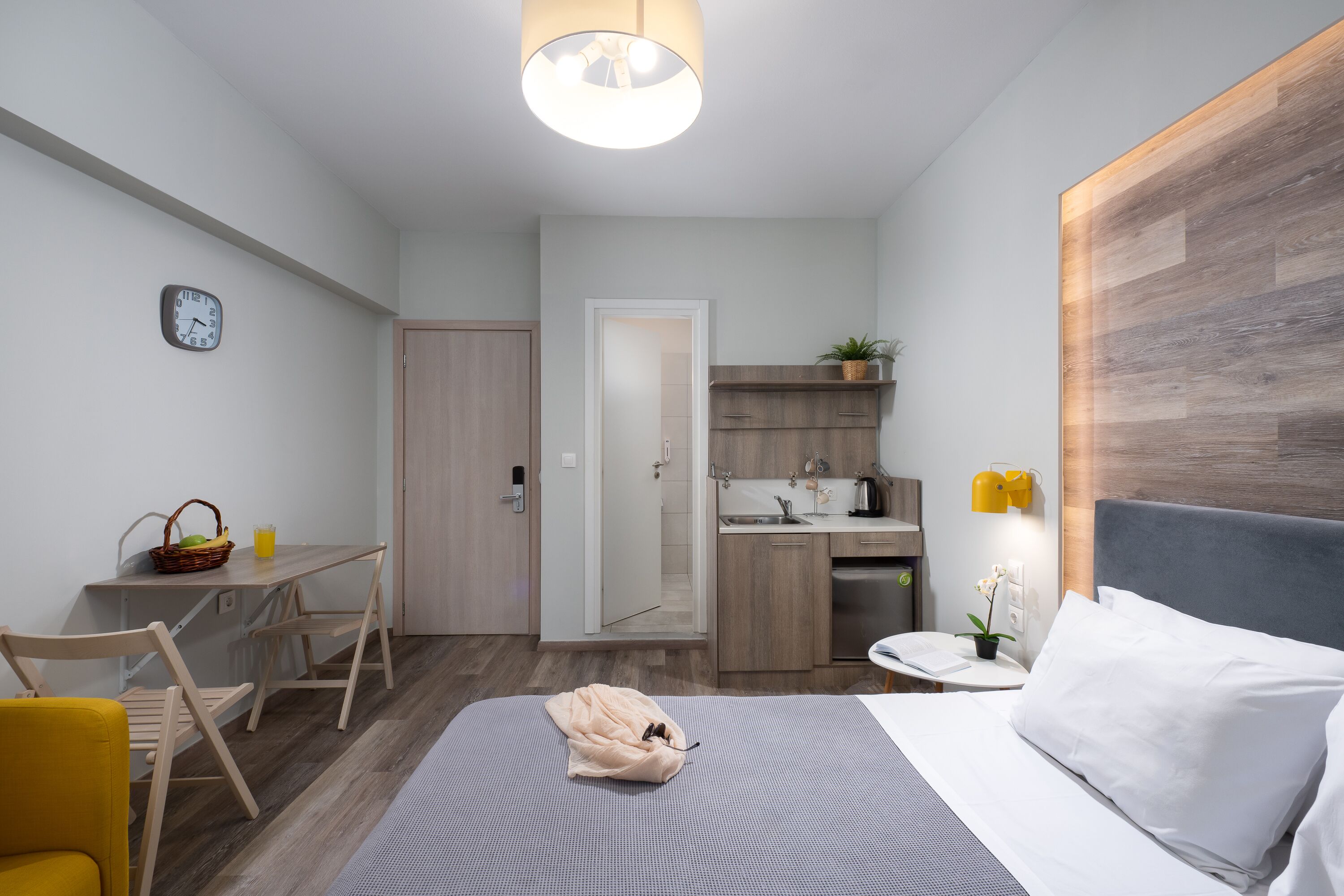 A modern hotel room with a bed, a desk, and a kitchenette.