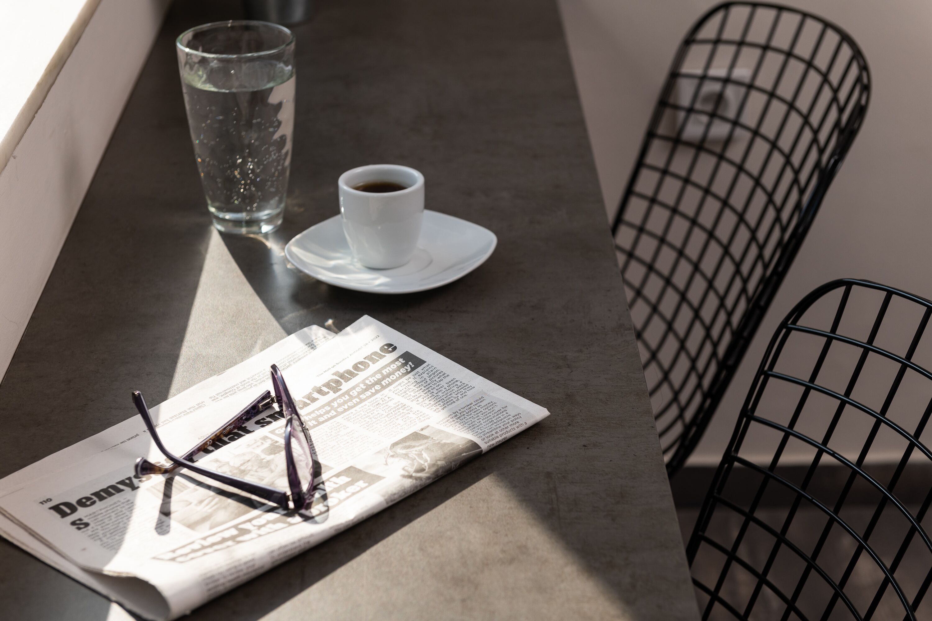 A newspaper, a cup of coffee, and a pair of glasses on a table.