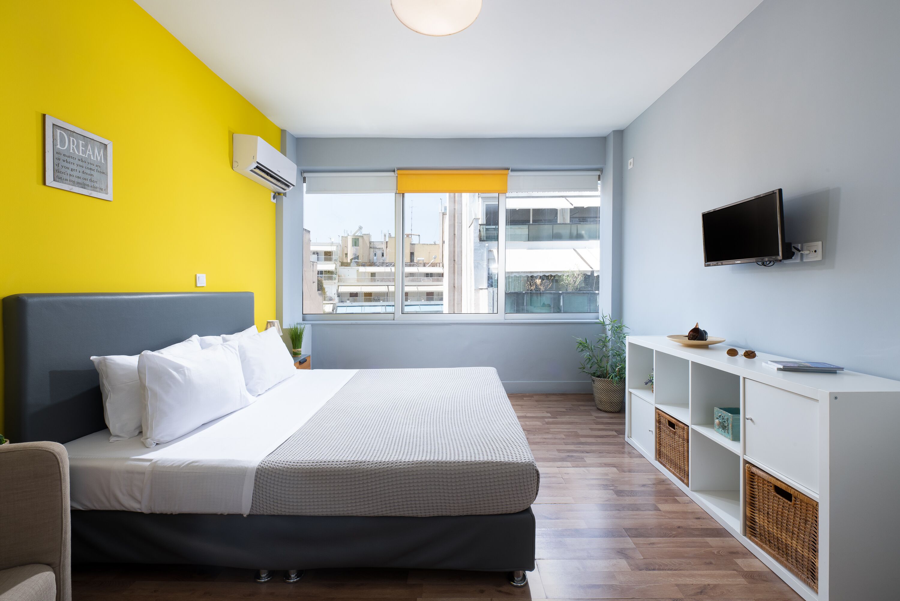 A modern bedroom with a bed, a TV, and a window with a view of buildings.