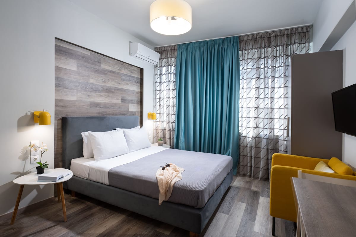 A modern hotel room with a large bed, a small table with a lamp, a TV, and a yellow chair.
