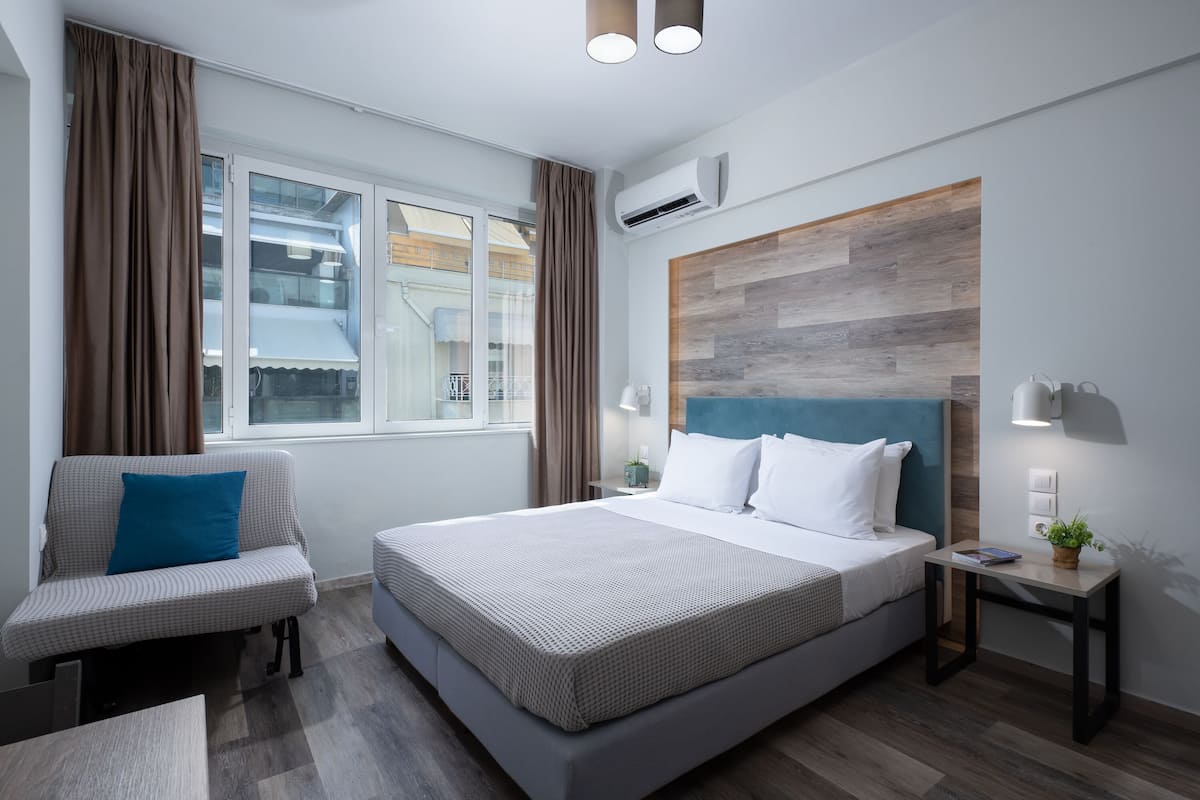 A modern hotel room with a large bed, a sofa, a small table, and a window with curtains.