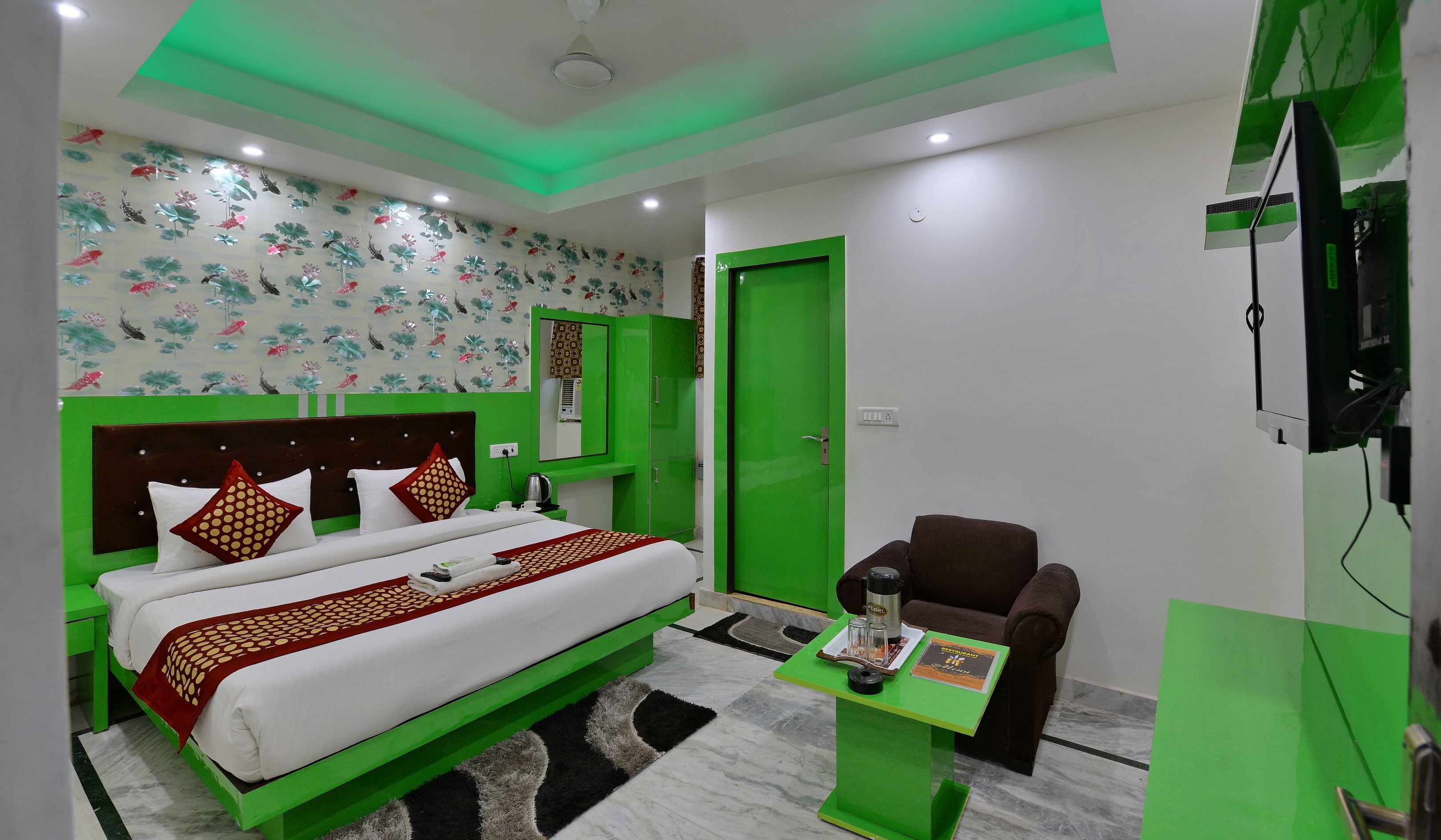 A hotel room with a bed, green accents, a green chair, a small table, and a television.