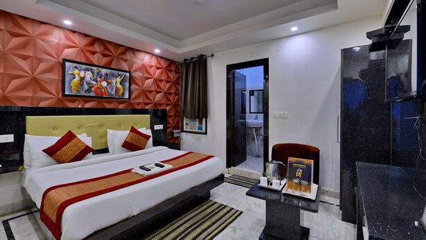 A hotel room with a bed, a desk with a coffee maker, and a view of the bathroom. - Hotel Noida International (Noida)