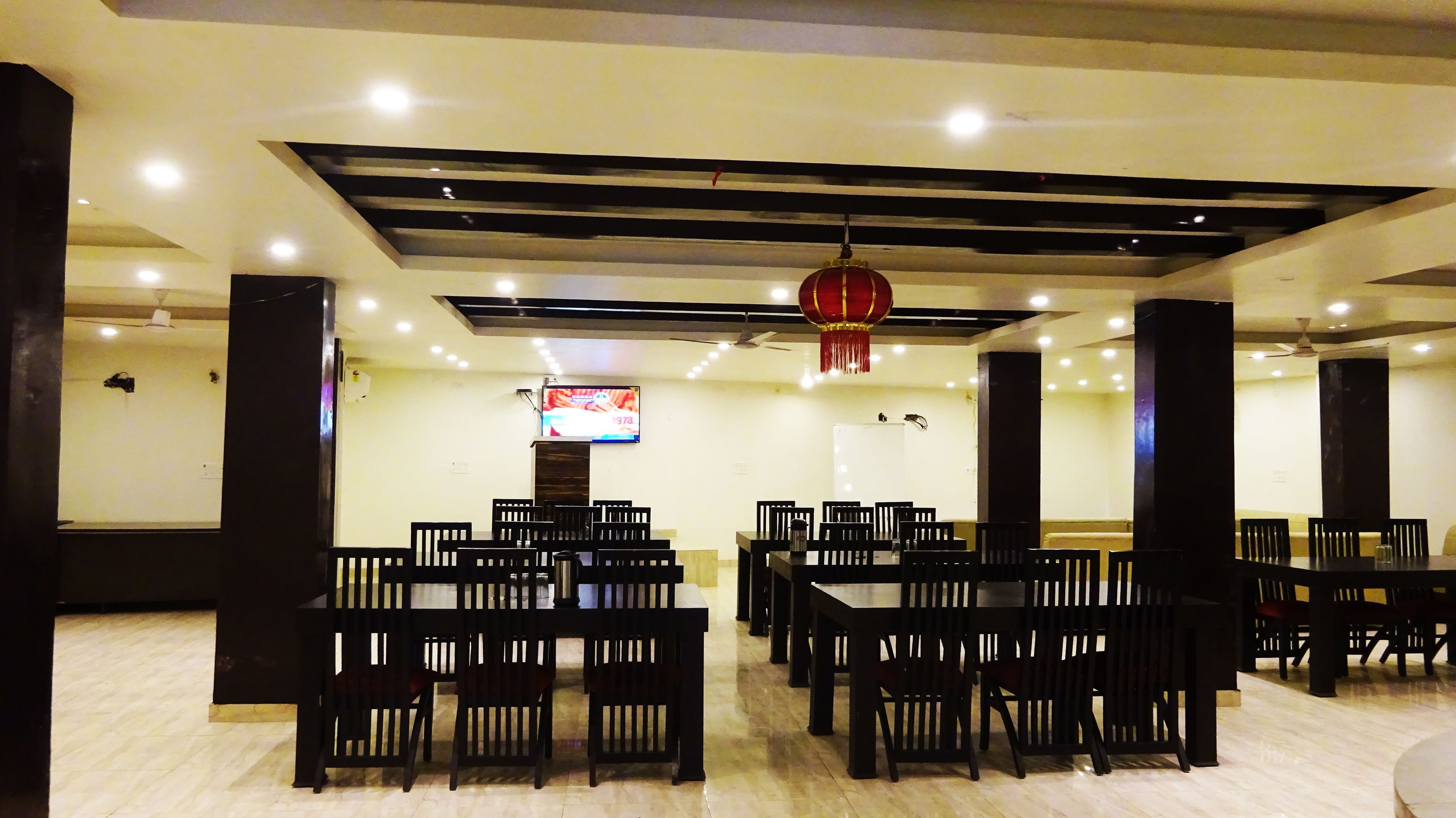 A spacious dining area with multiple tables and chairs, a ceiling fan, recessed lighting, and a television screen.