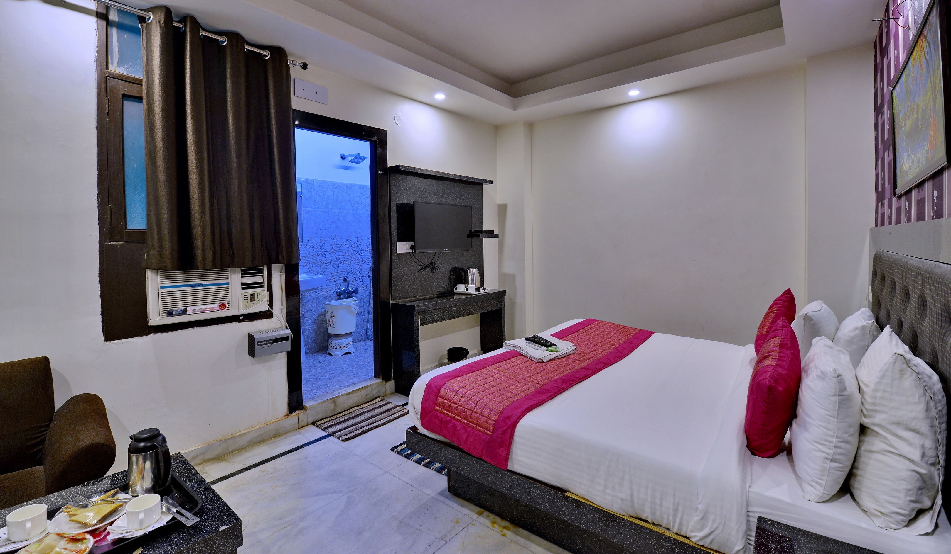 A hotel room with a bed, a desk, a television, a bathroom, and a window with curtains.