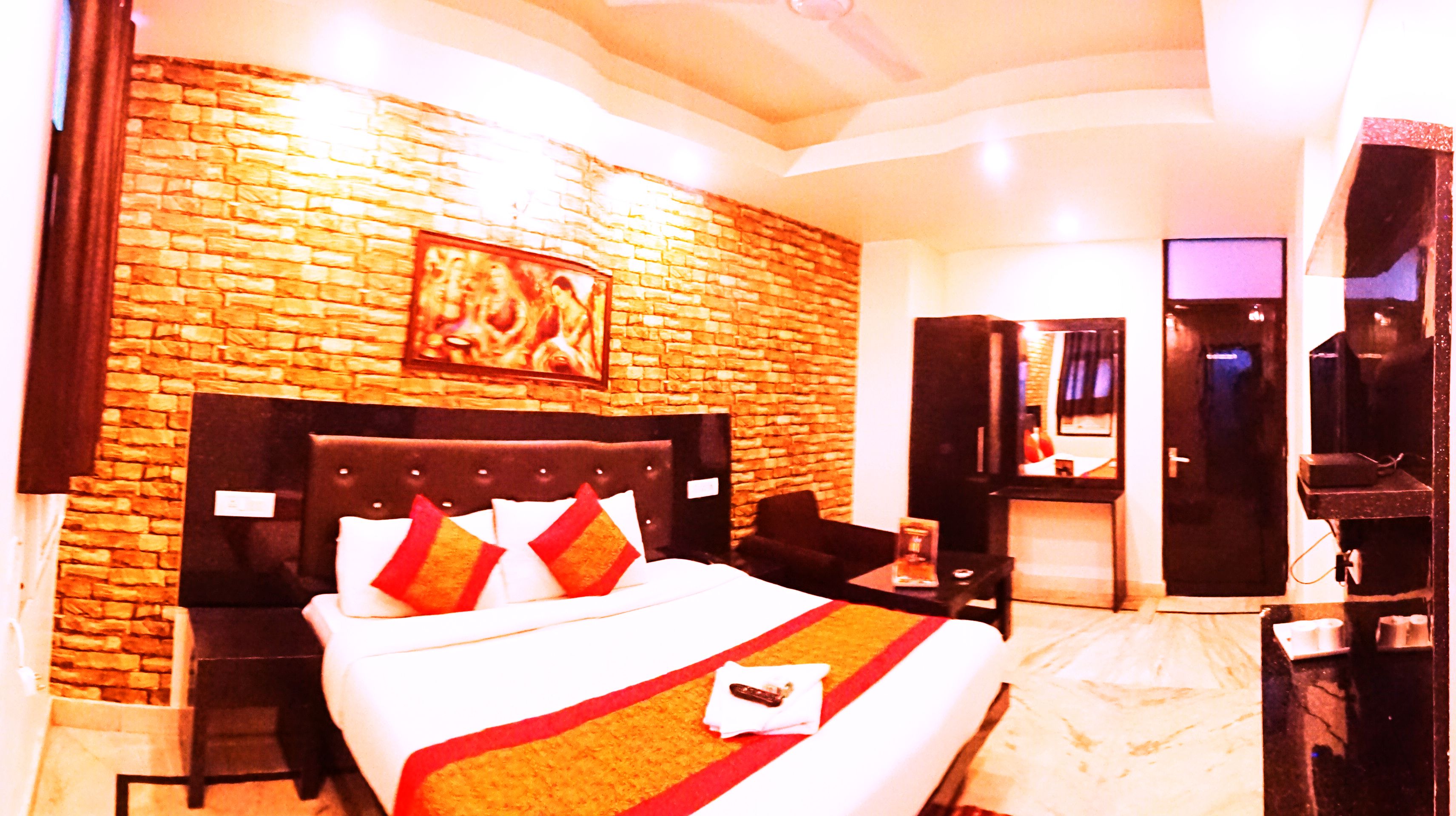 A hotel room with a brick wall, a large bed with red and white bedding, a flat-screen TV, a desk, and a mirror.