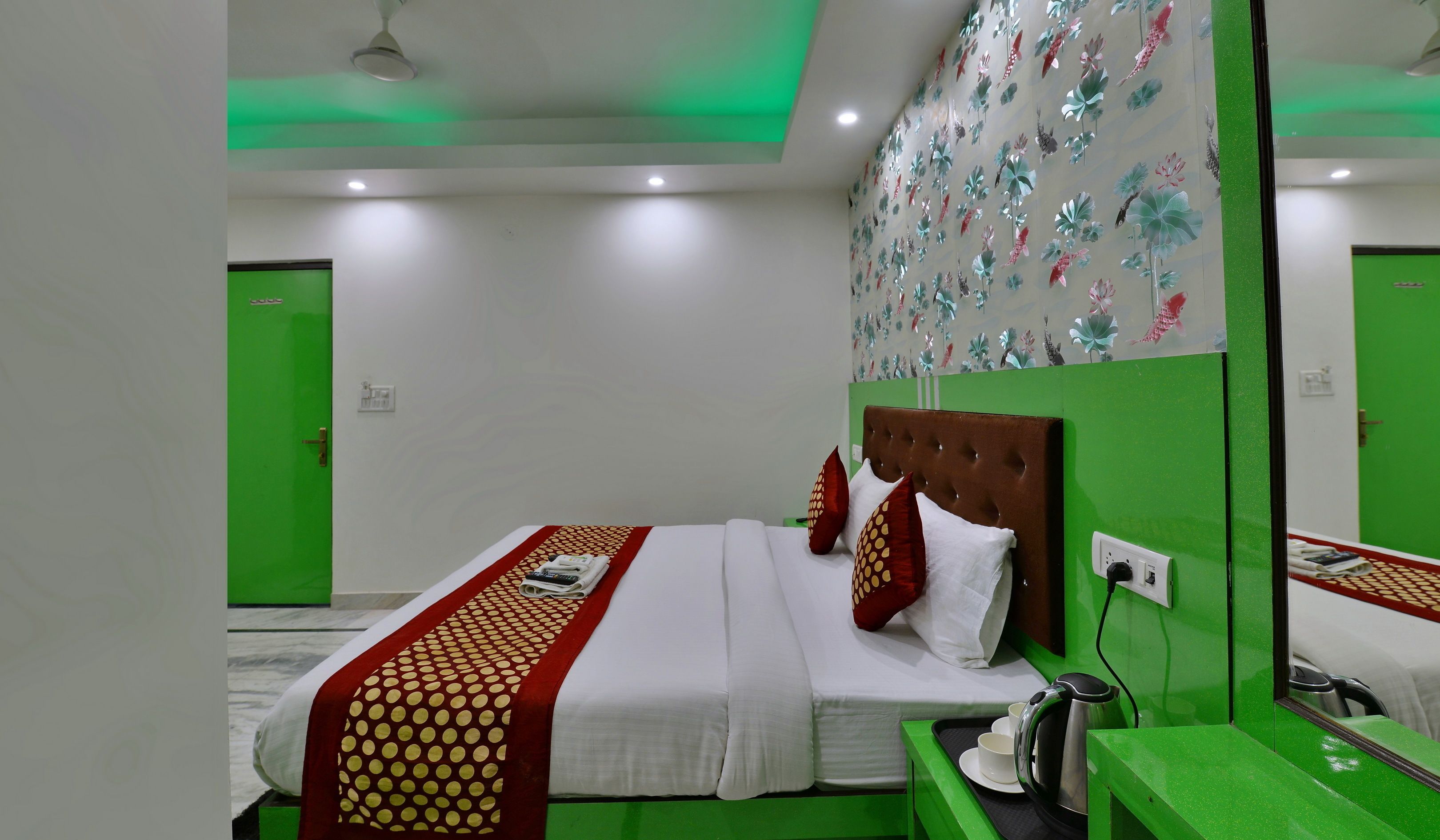 A hotel room with a bed, green walls, a mirror, and a ceiling with green lighting.