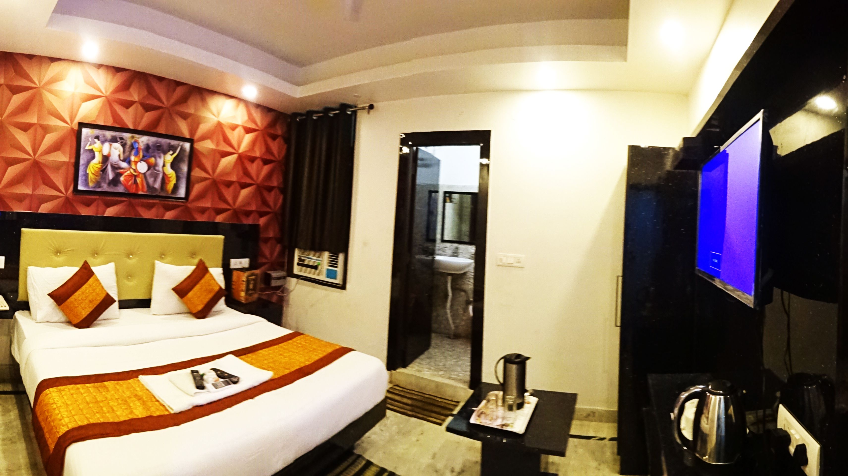 A hotel room with a large bed, a flat-screen TV, a coffee maker, and a bathroom visible through an open door.