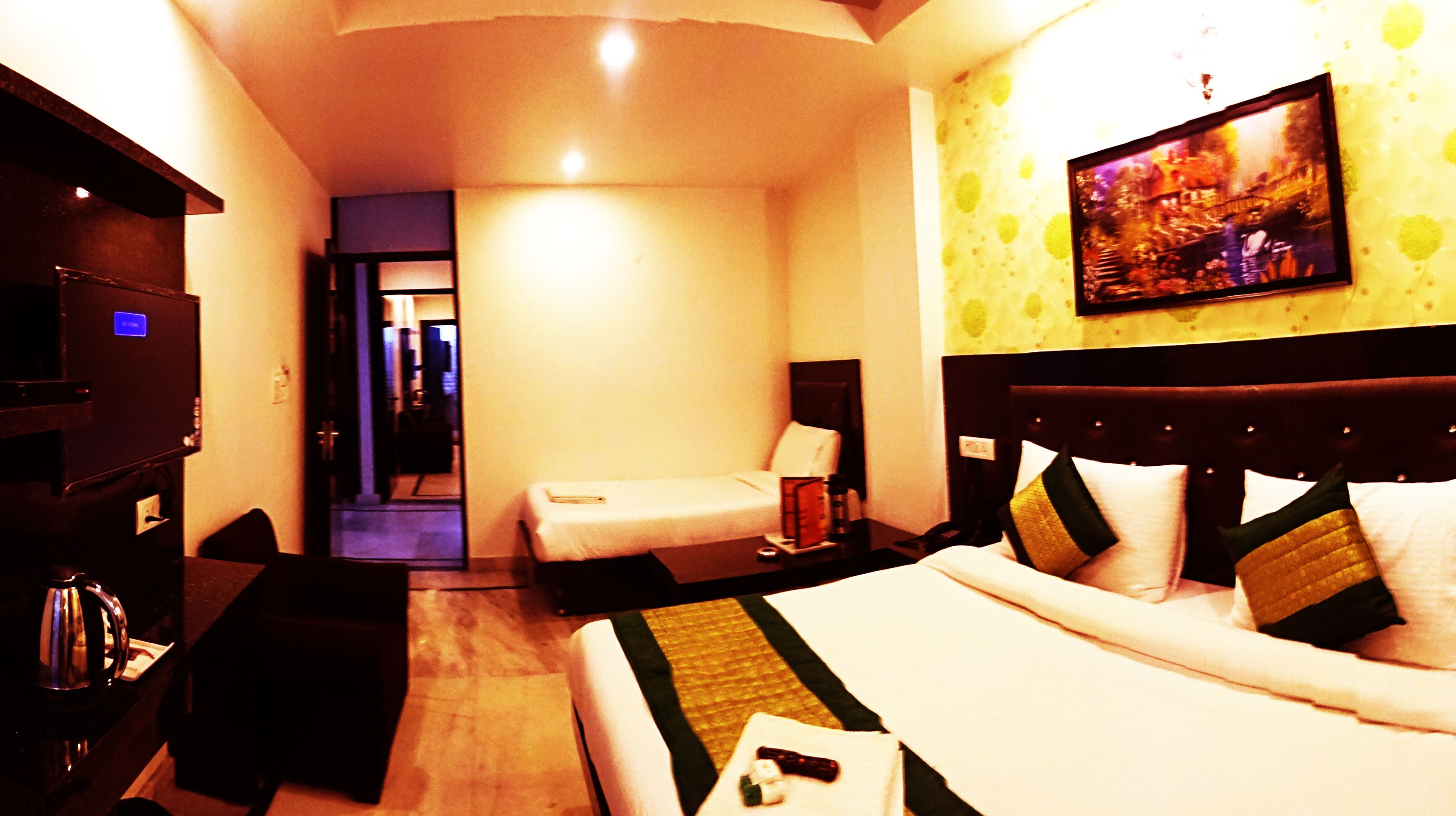 Habitación de hotel con cama, escritorio, silla, televisor y un cuadro en la pared.