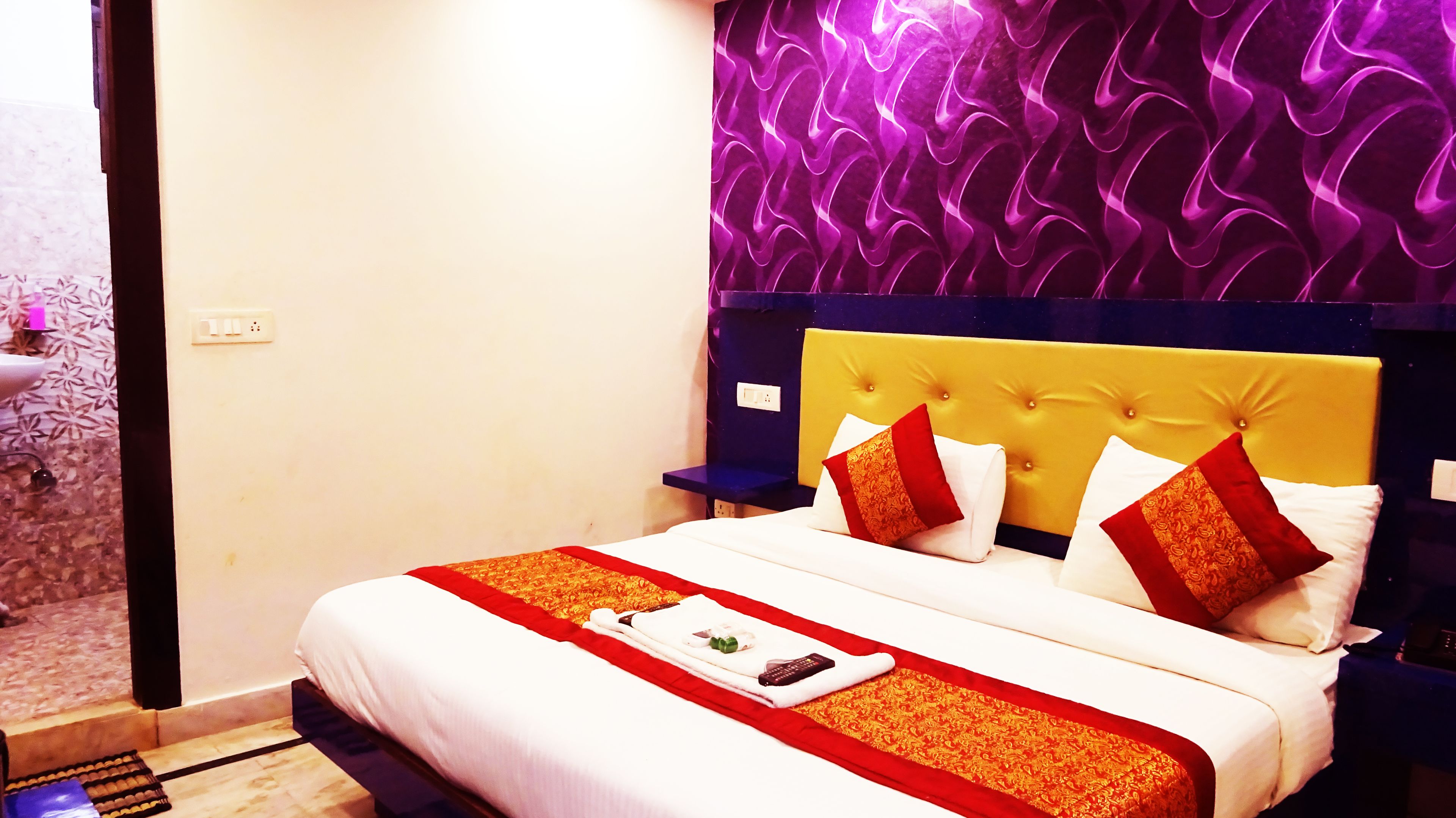 A hotel room with a bed, a bedside table, and a wall with a purple wavy pattern.