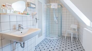 A modern bathroom with a white sink, a glass shower enclosure, and a chair.