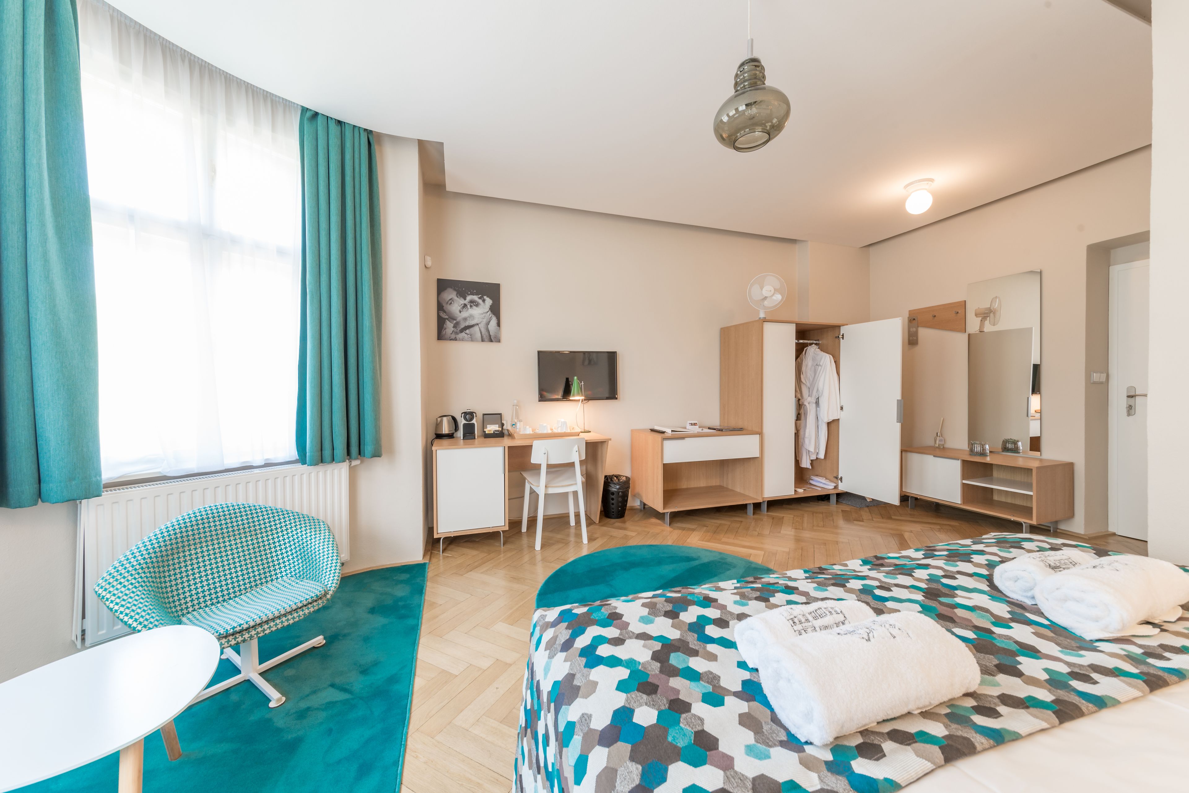 A modern hotel room with a bed, a desk, a chair, and a wardrobe.