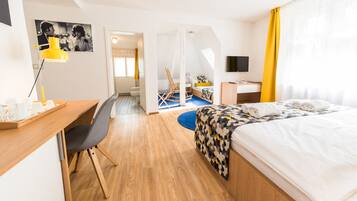Una habitación de hotel moderna con un escritorio de madera, una cama con una colcha estampada, un televisor y un baño visible a través de una puerta abierta.