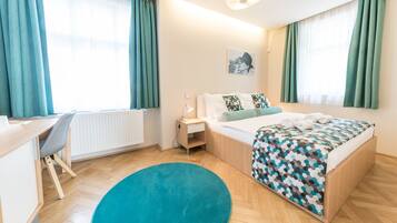 A hotel room with a bed, a desk, a chair, a nightstand, and a large window with curtains.