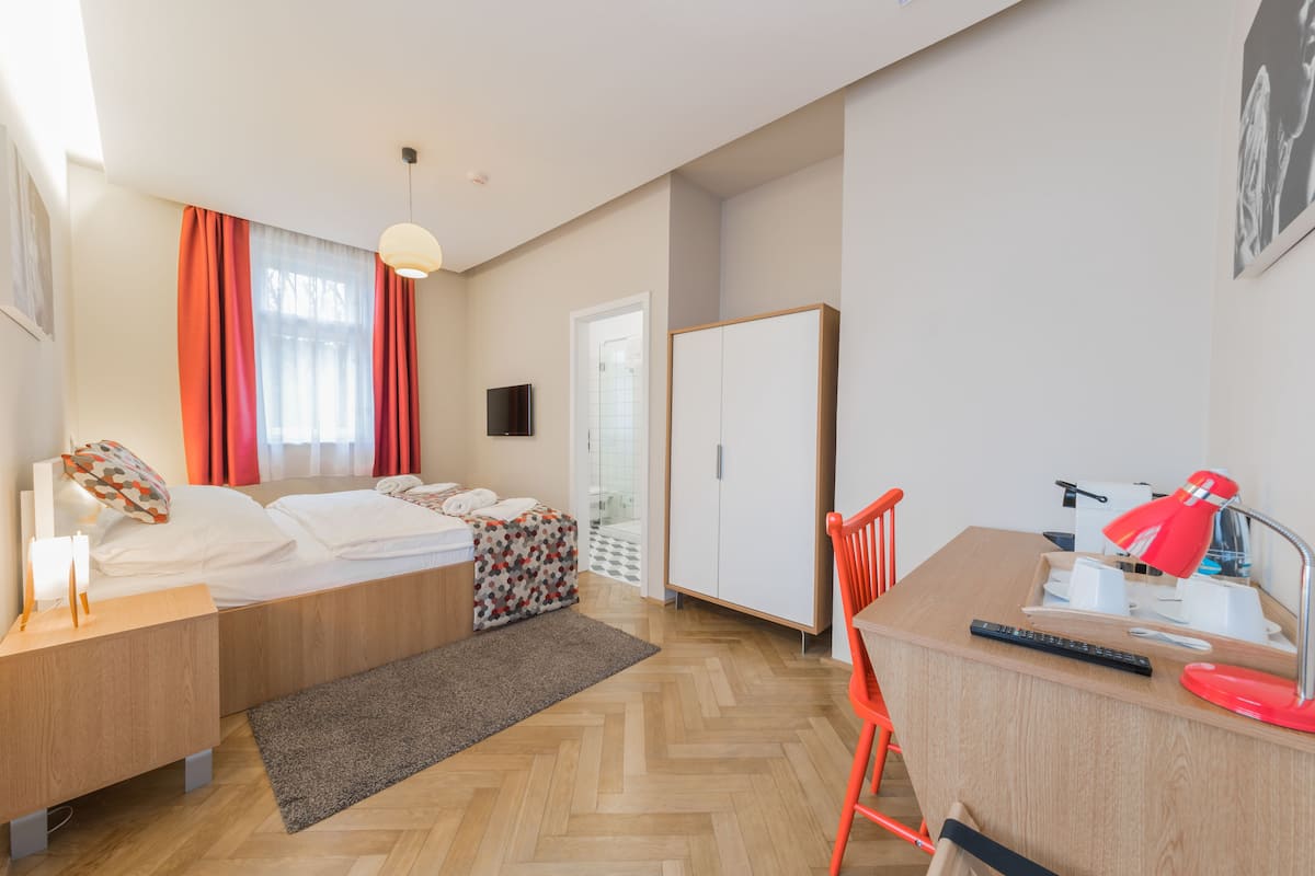 A modern hotel room with a bed, desk, chair, and wardrobe.