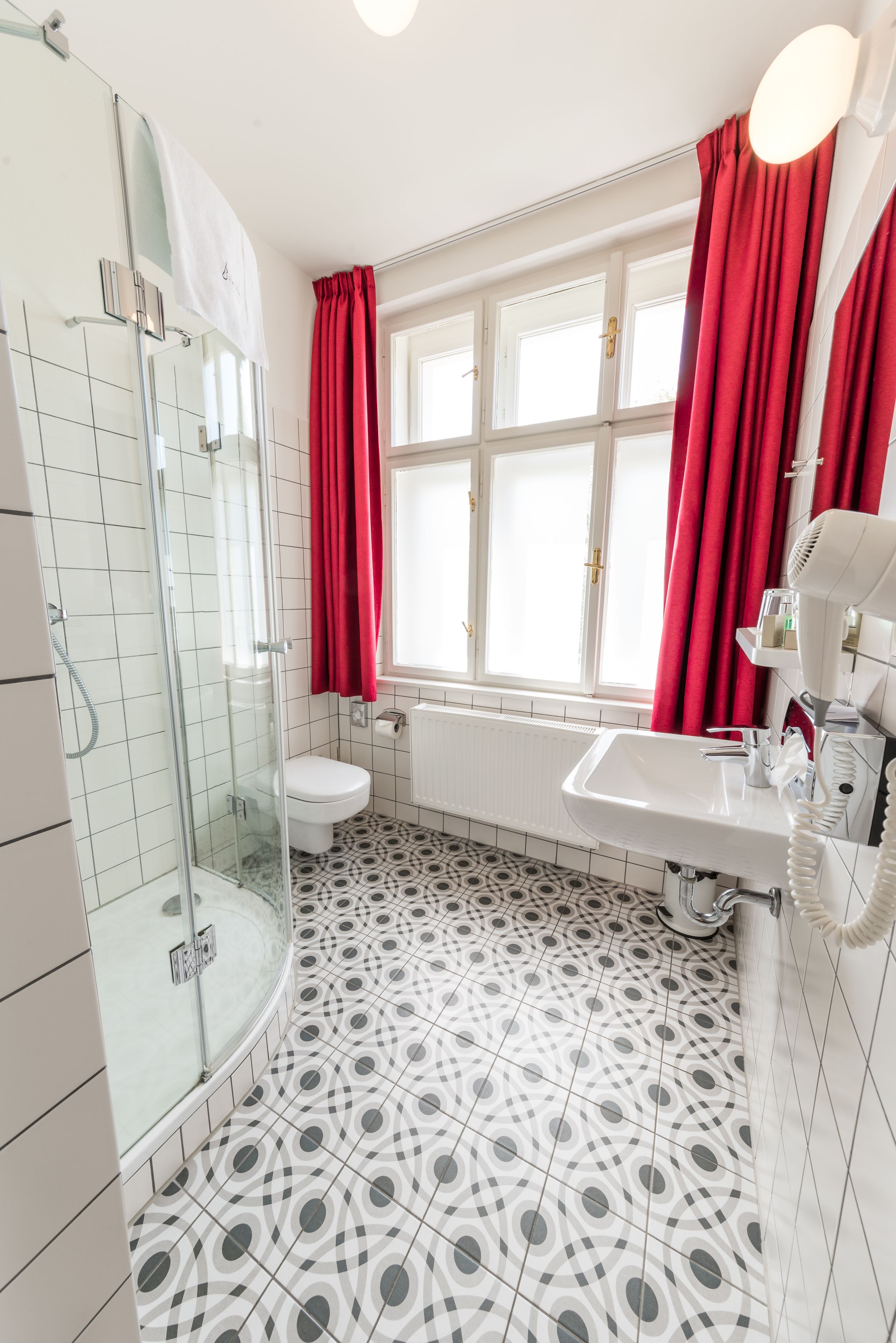 Casa de banho com chuveiro envidraçado, sanita branca, banheira e lavatório com secador de cabelo.