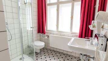 Casa de banho com chuveiro envidraçado, sanita branca, banheira e lavatório com secador de cabelo.