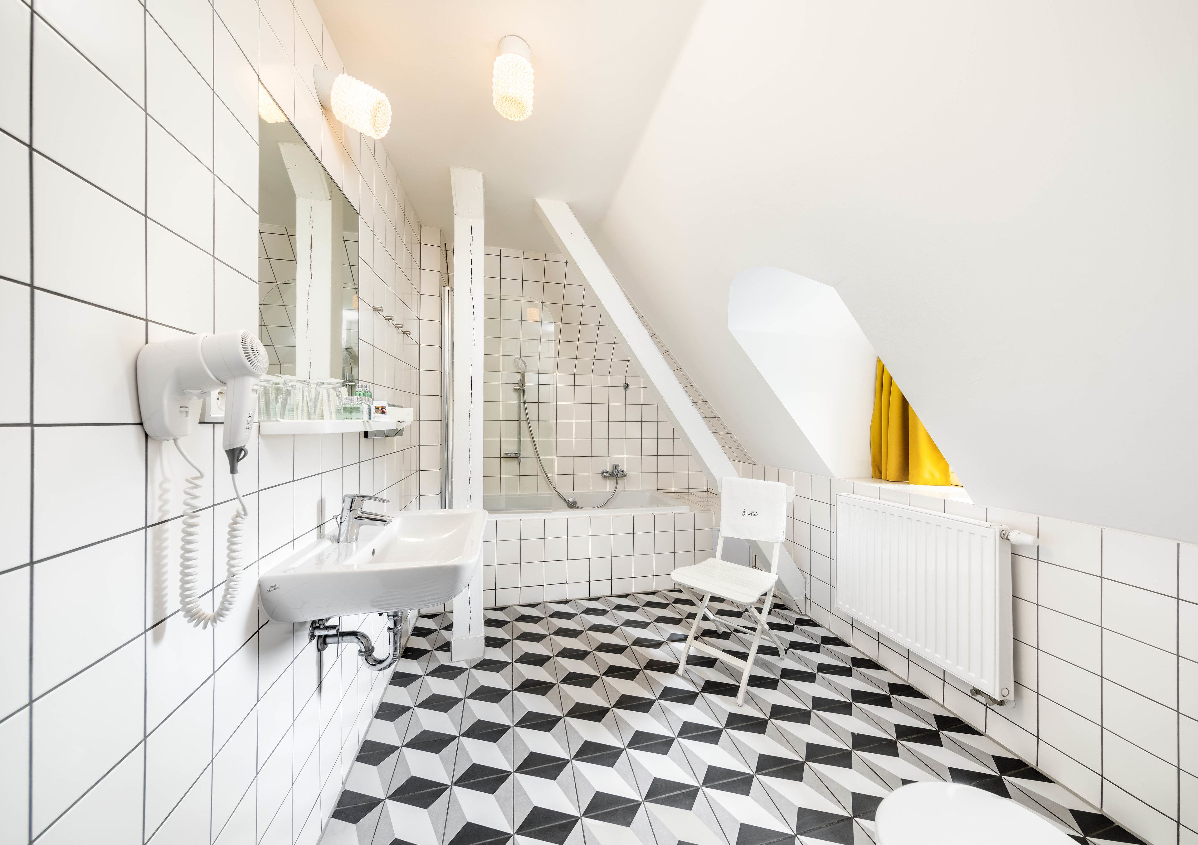 Un baño moderno con suelo a cuadros blanco y negro, un lavabo blanco, un secador de pelo, una ducha y un radiador.