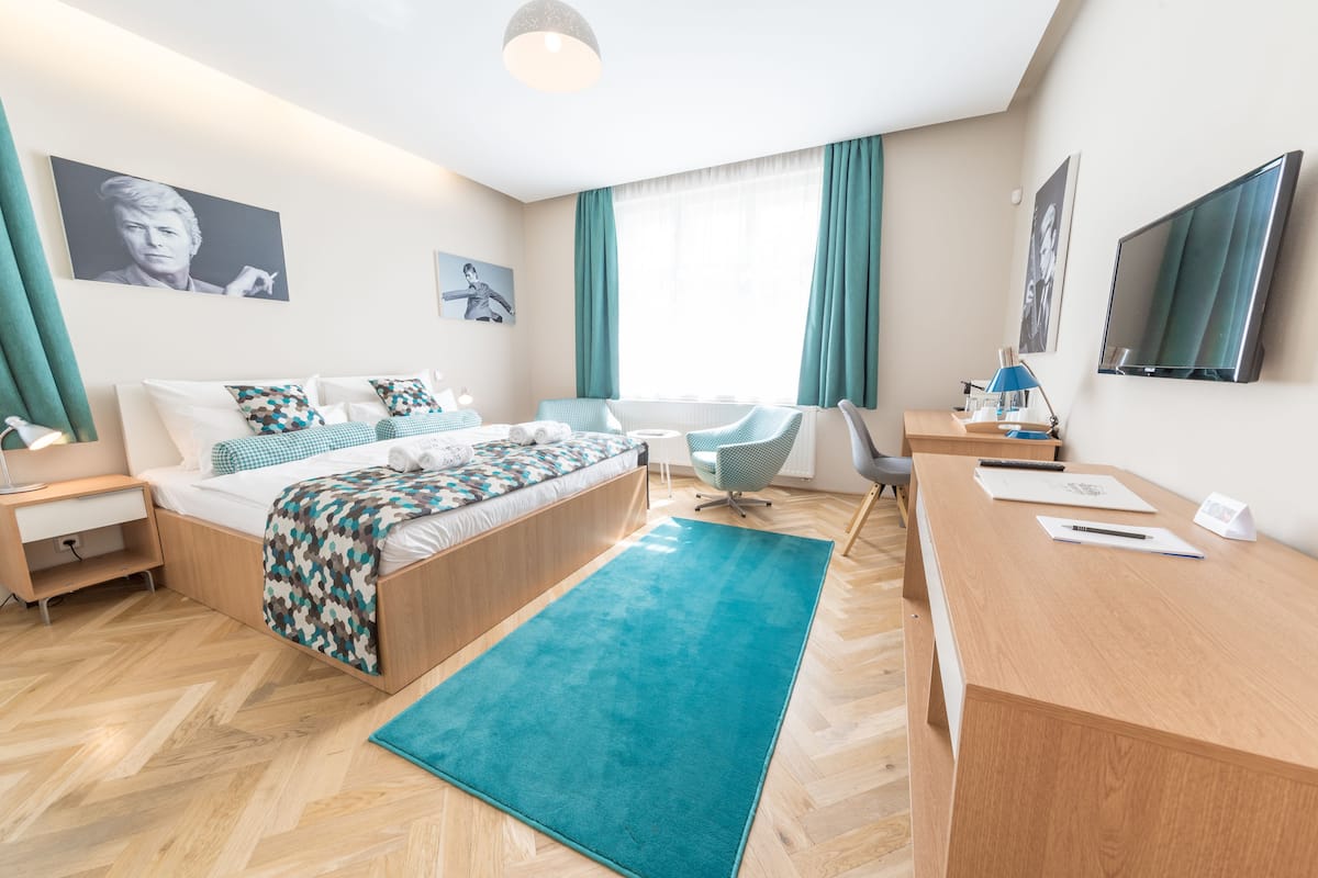 A modern hotel room with a bed, desk, chair, and artwork on the walls.