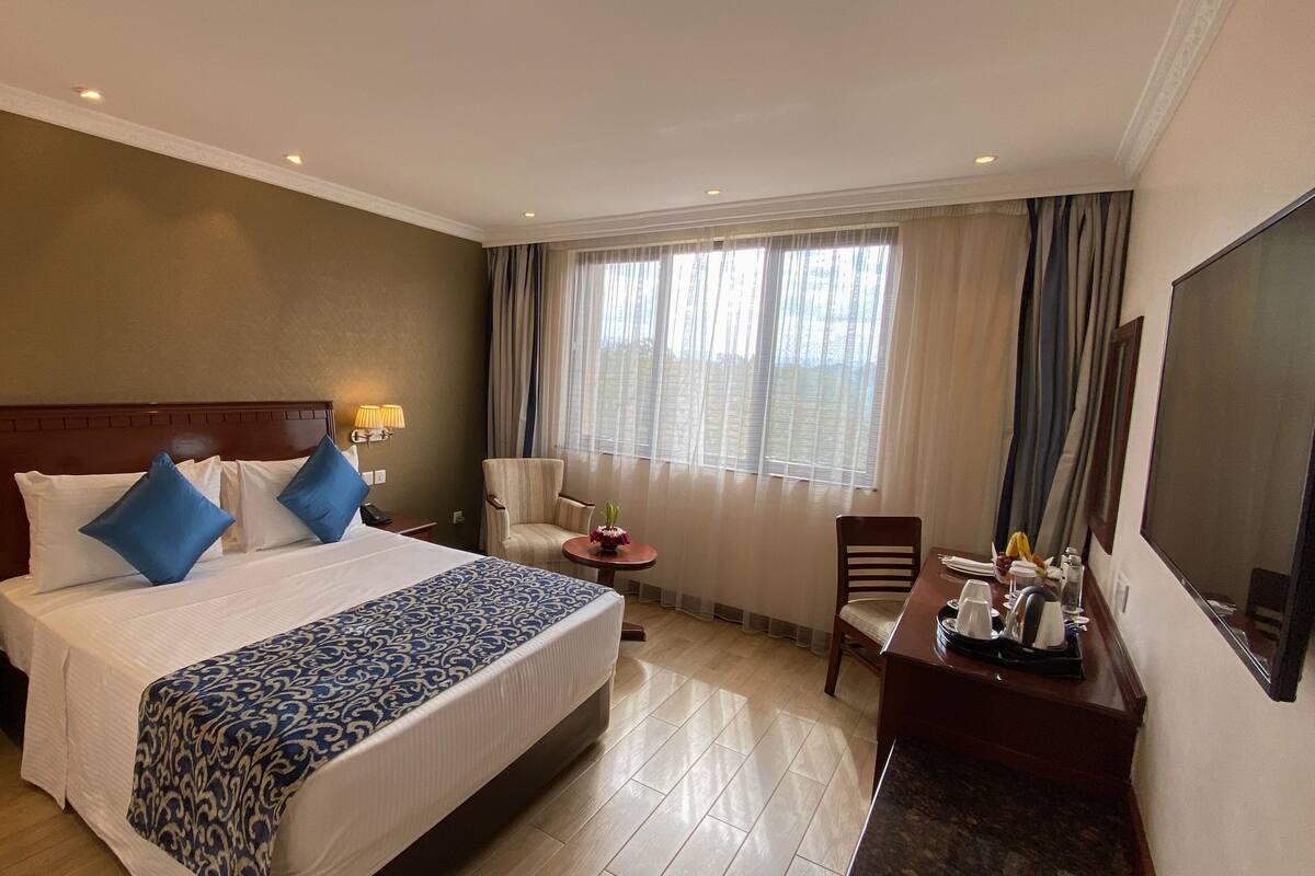 Une chambre d’hôtel avec un grand lit, un bureau, une chaise, une télévision et une fenêtre avec des rideaux.