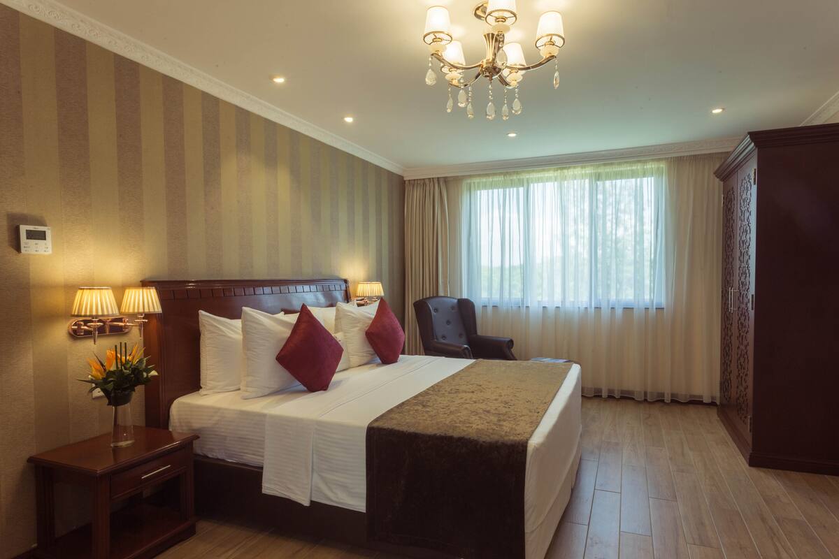 Une chambre d’hôtel avec un grand lit, une chaise, une table de chevet avec des lampes et une armoire.