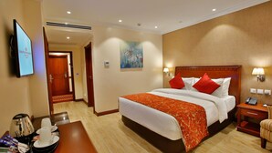 Habitación de hotel con una cama grande, un televisor, un escritorio con una bandeja de alimentos para el desayuno y un cuadro en la pared.