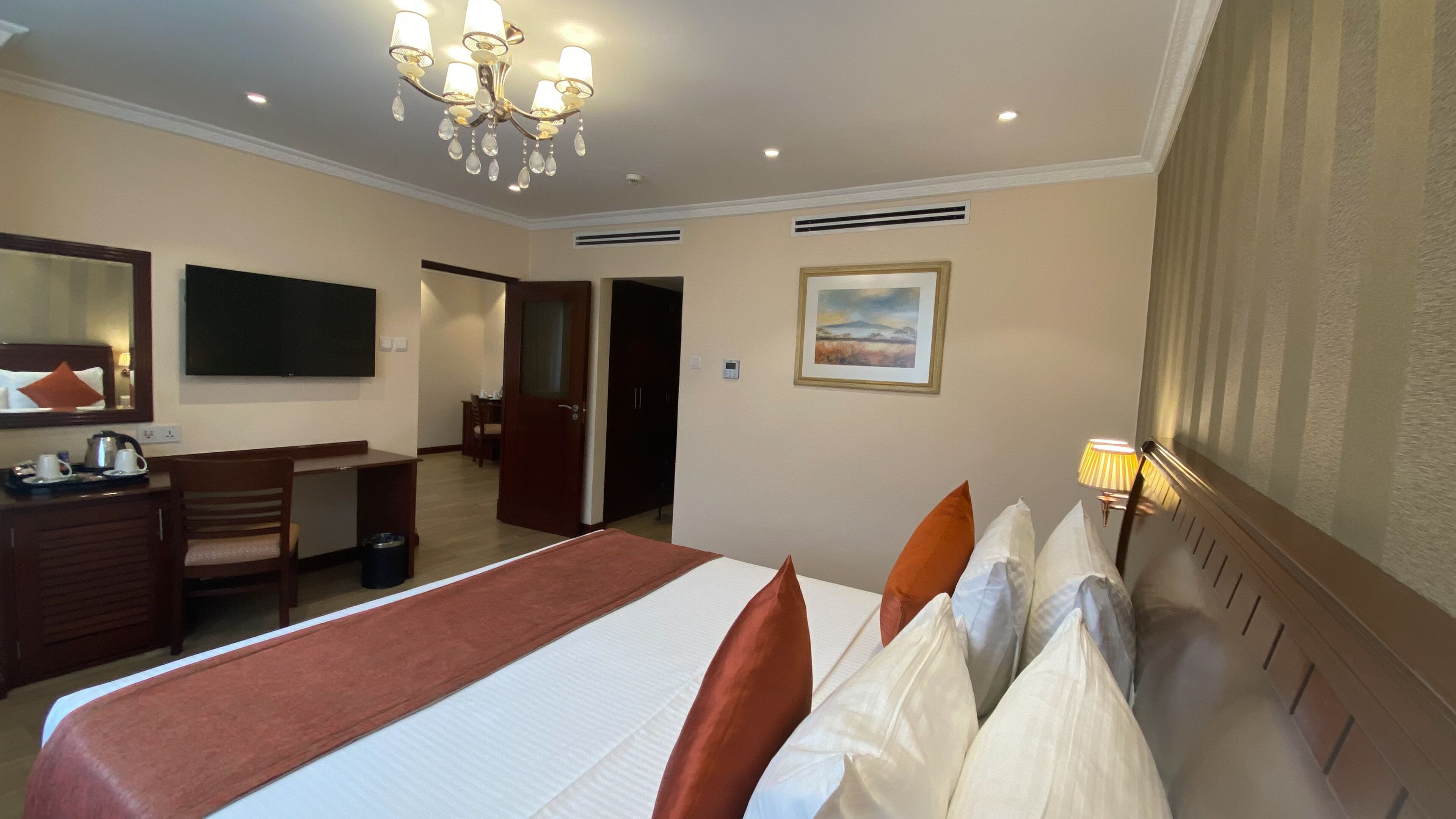 A hotel room with a large bed, a desk, a chair, a TV, and a painting on the wall.