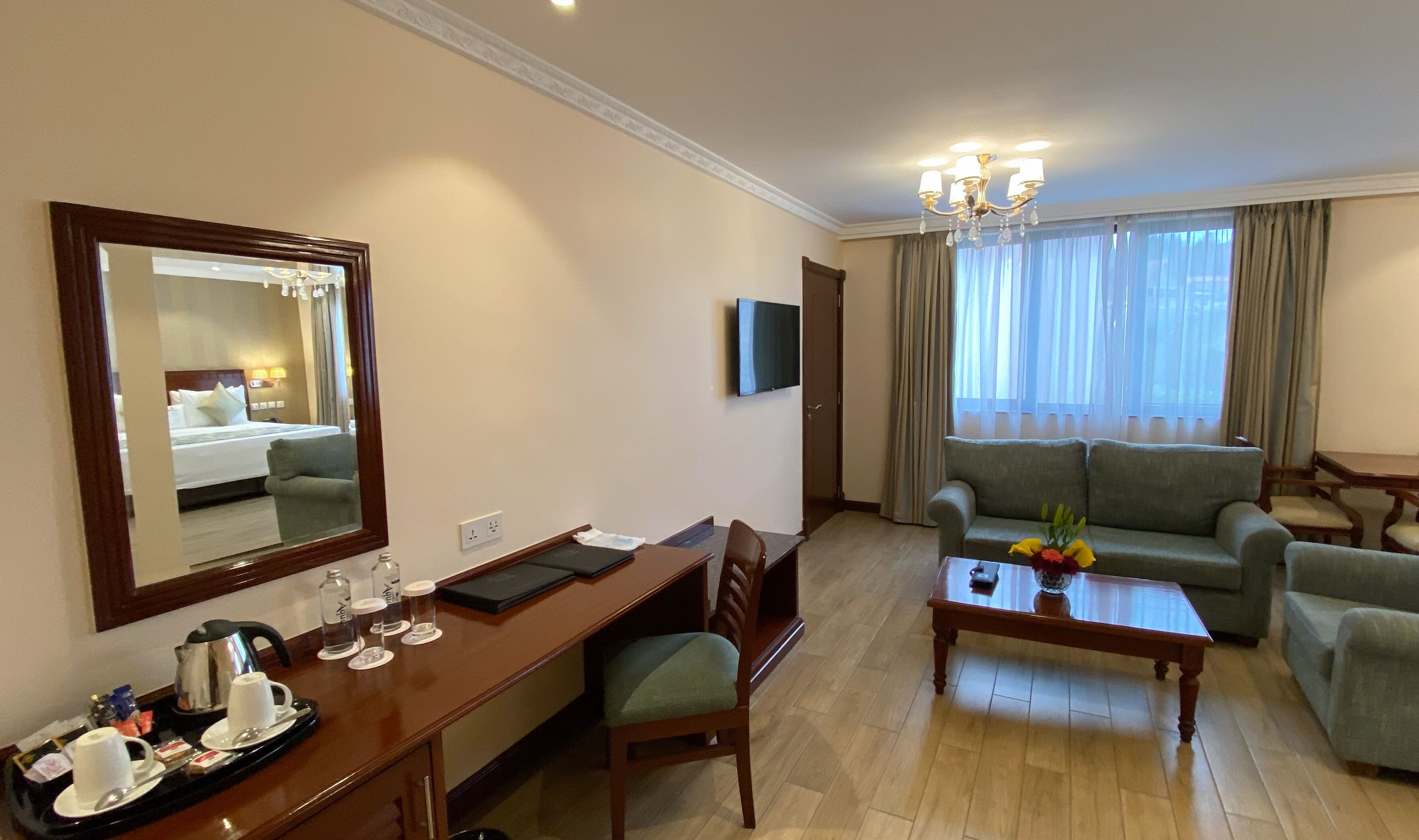 Quarto de hotel com cama, escrivaninha com cadeira, sofá, mesa de centro e televisão.