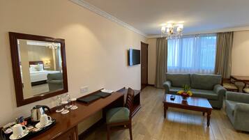 A hotel room with a bed, a desk with a chair, a sofa, a coffee table, and a TV.